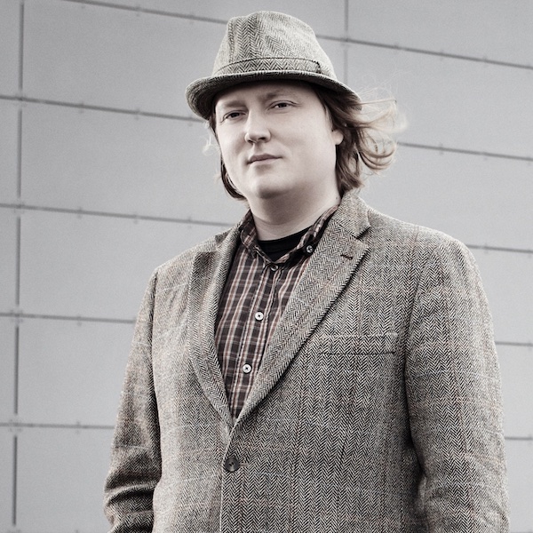 Male looking intently at camera wearing tweed jacket and hat